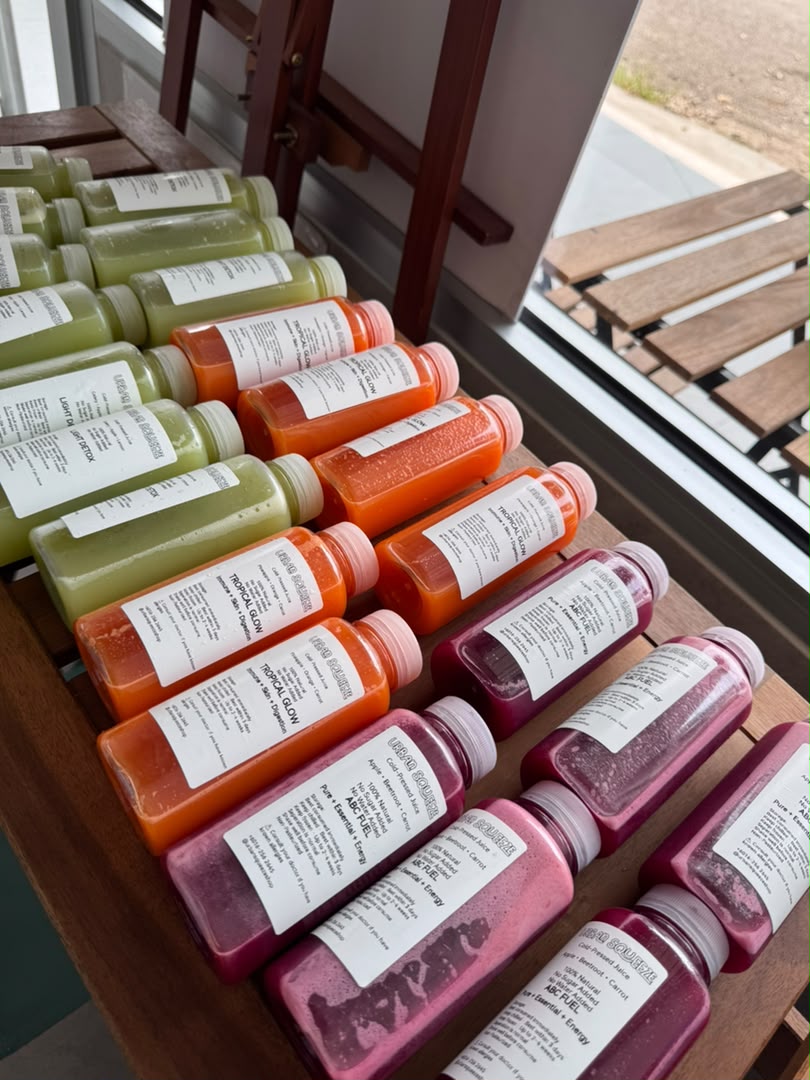 Rows of green, orange and red cold-pressed juice bottles on a wooden table by the window