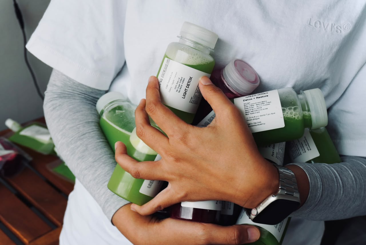 A person in a white top holding several green and red cold-pressed juice bottles
