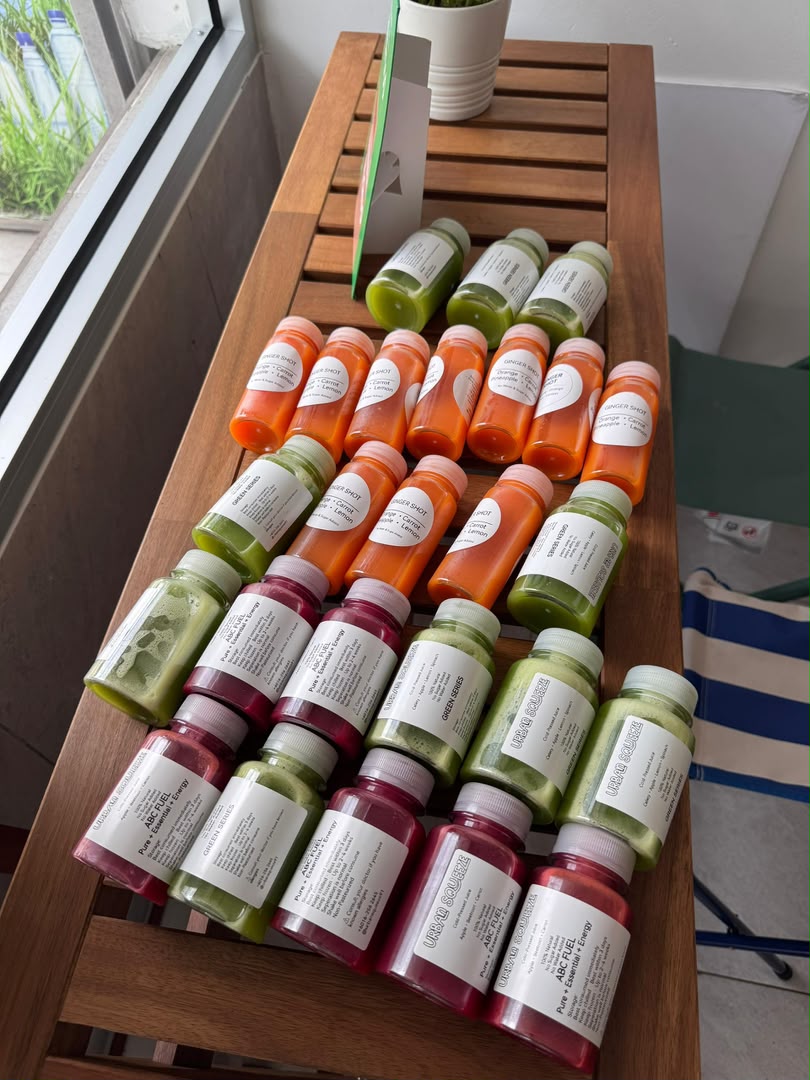 A large batch of orange, green and red juice bottles arranged in rows across a wooden table