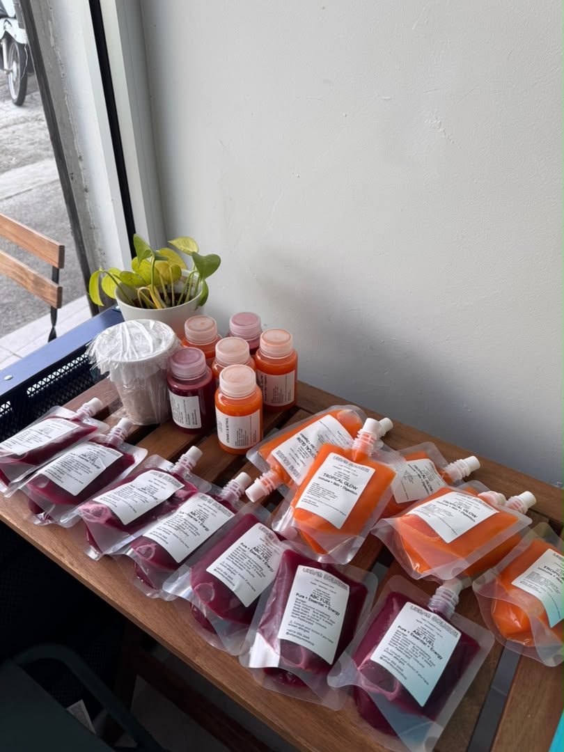 Red and orange juice pouches spread across a wooden table with bottles behind them