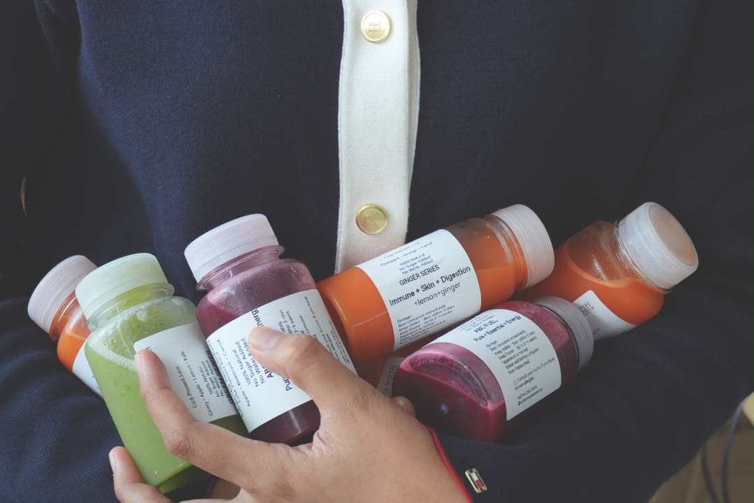 A person in a navy top holding orange, green and red cold-pressed juice bottles