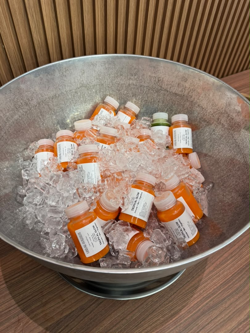 Mostly orange Tropical Glow juice bottles chilled on ice in a large metal bucket