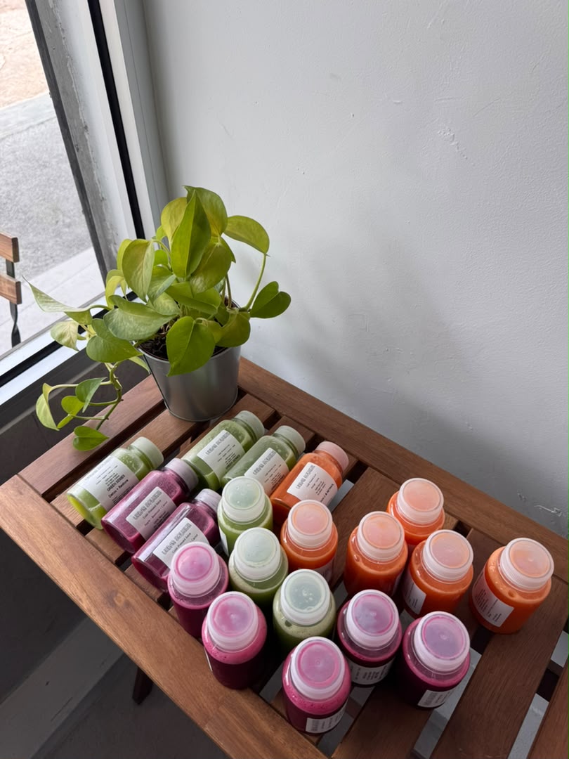 Mixed orange, green and red juice bottles arranged beside a potted plant on a wooden table