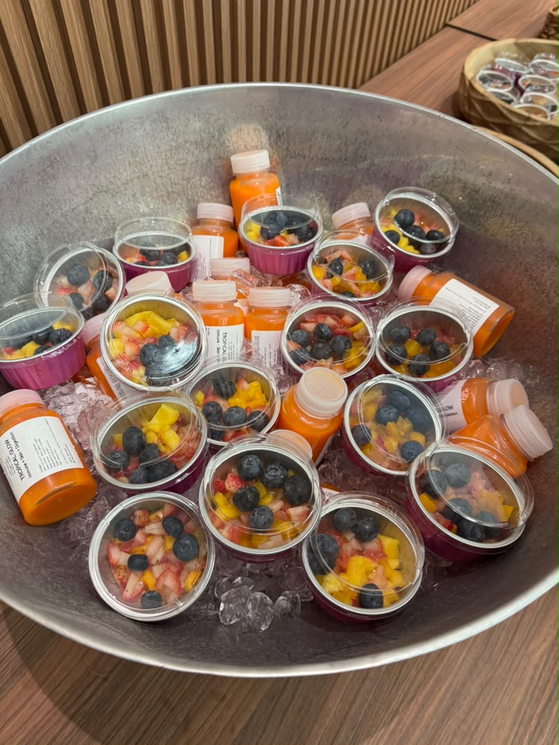 Cups of cut fruit and orange juice bottles served on ice in a large metal bucket