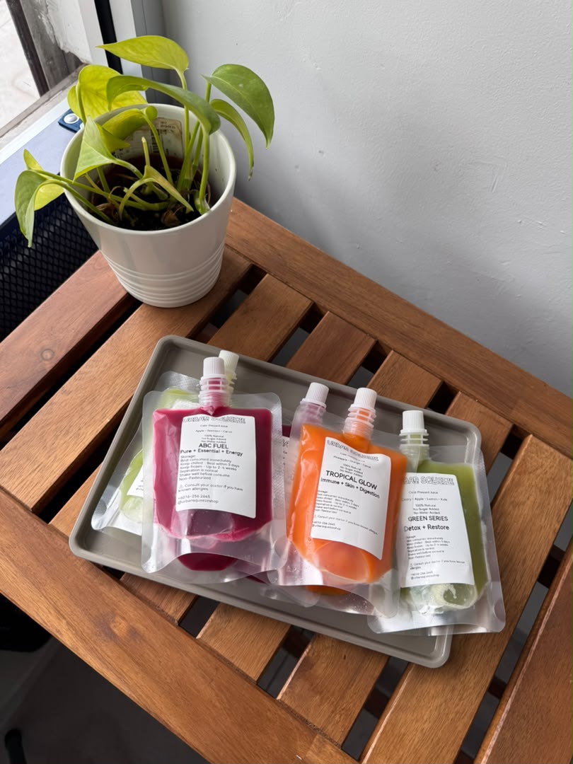 ABC Fuel, Tropical Glow and Green Series juice pouches on a tray beside a potted plant