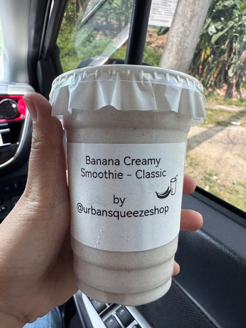 A hand holding a Banana Creamy Smoothie Classic cup inside a car