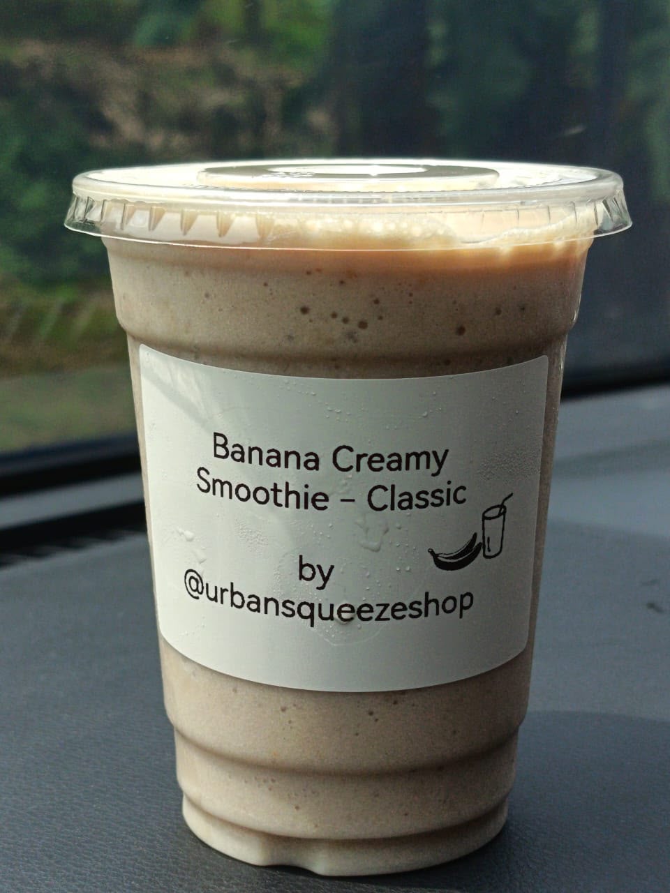 A Banana Creamy Smoothie Classic cup standing on a car dashboard