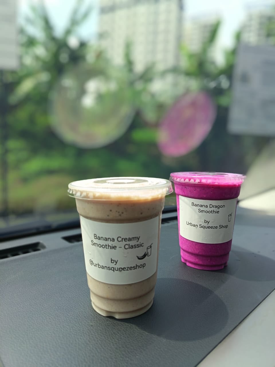 Banana Creamy and bright pink Banana Dragon smoothie cups together on a car dashboard